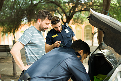 Worried caucasian man waiting for the cops to search his car trunk while searching for a criminal evidence